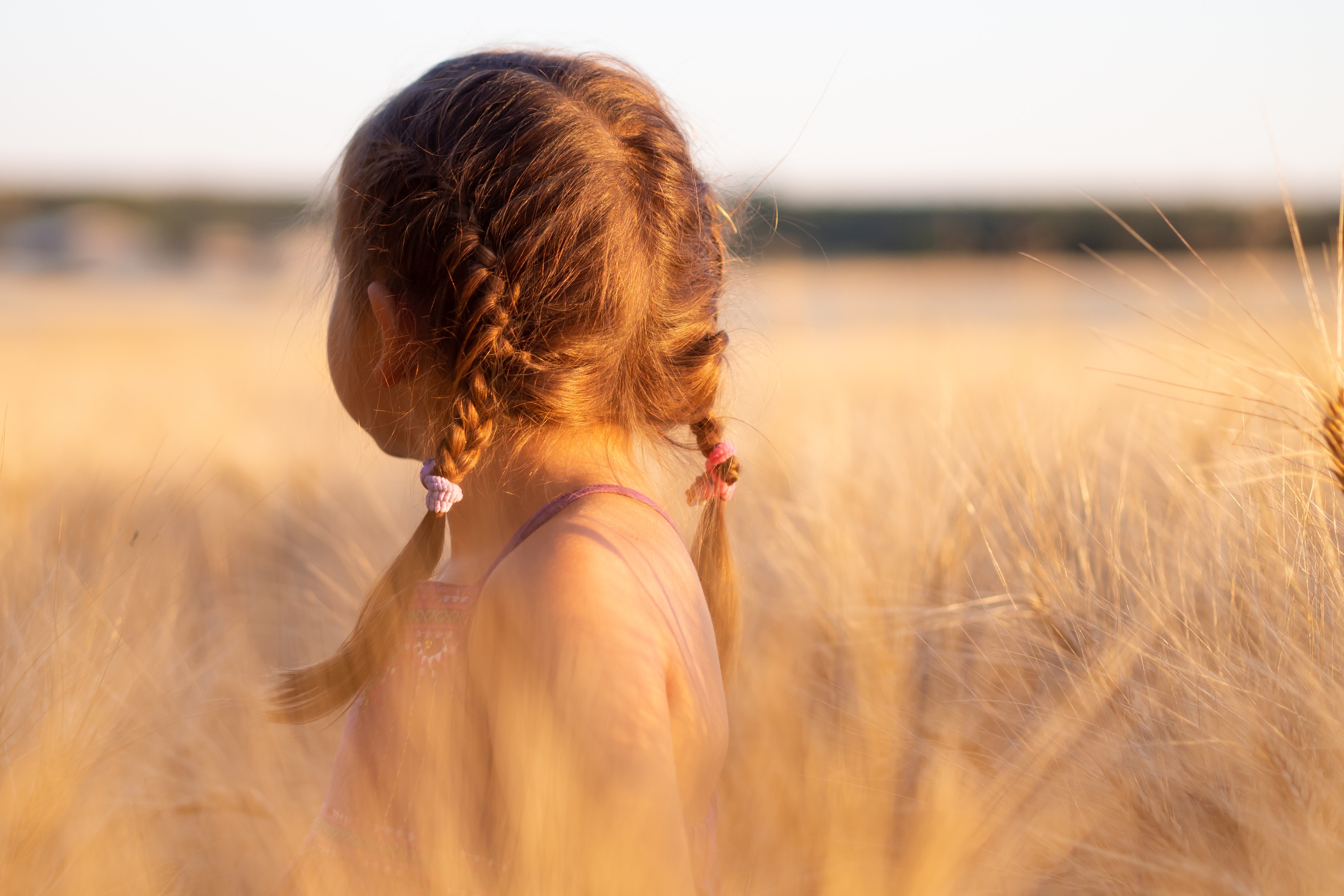 En liten jente ute i gresset med fine fletter i håret